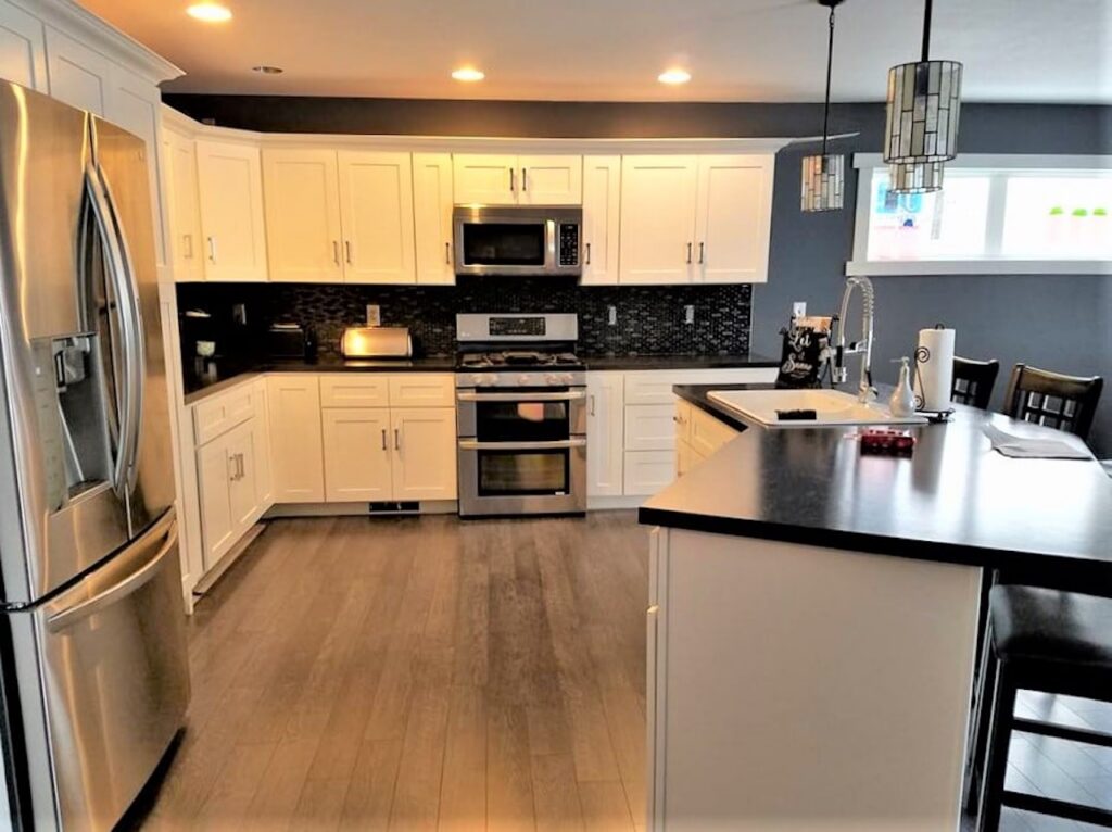 Finished modern kitchen with white cabinetry, stainless steel appliances, black granite countertops, and island seating