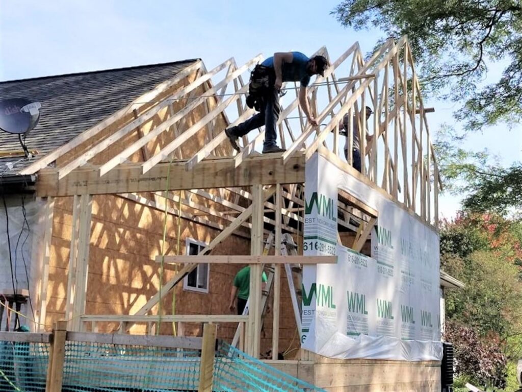 Construction worker installing roof framing on a home addition with wooden trusses and WML brand house wrap