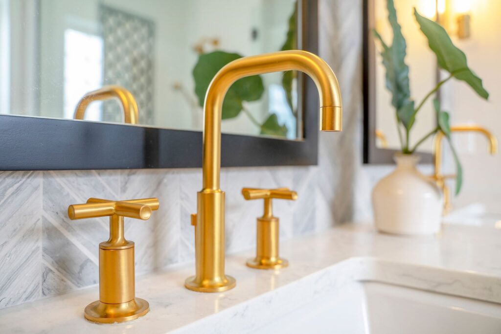 Modern bathroom vanity with gold faucet fixtures, marble countertop, vessel sink, and potted green plant